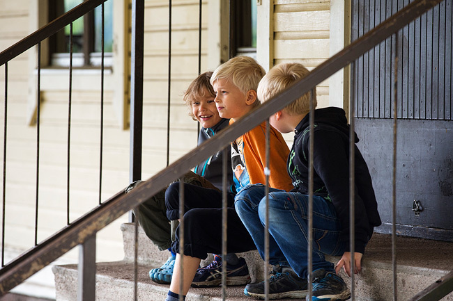 Kolme poikaa istumassa koulun portailla